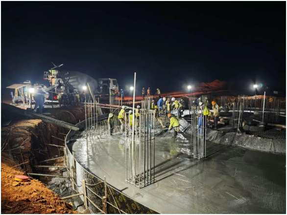 当地时间5月23日,武黄公司安胜矿业项目传来捷报,选矿系统核心单元之一—3号浓密机底板混凝土顺利浇筑完成。本次施工混凝土总方量约500立方米,连续作业30小时圆满收官,标志着该结构节点施工任务顺利完成,为后续设备安装打下坚实基础。 3号浓密机作为选矿车间的重要设施,其底板结构钢筋密集、布筋复杂,且对平整度、强度等级等质量指标要求极高,施工组织协调难度大。为确保浇筑顺利推进,该项目部提前召开专题策划会议,优化施工组织方案,明确各环节责任人,重点加强混凝土供应调度、泵送路径布设、连续浇筑控制和现场照明布置。 施工期间,技术人员全程驻点旁站,严格把控混凝土振捣、收面压光与养护等工作,确保混凝土浇筑均匀、密实、无离析,质量指标全面达标。同时,该项目部安排专人值守搅拌站,加强与搅拌站的协调联动,保证混凝土连续供应按时到场、泵送不中断,有效防止因供应失衡引发质量隐患。 此次3号浓密机底板的顺利浇筑,不仅为后续设备安装提供了坚实支撑,也为后续6台浓密机的施工积累了宝贵的组织经验与技术成果,在模板支设、钢筋绑扎优化、连续浇筑节奏控制等方面形成了可复制、可推广的工作机制。 下一阶段,项目部将以此为契机,总结经验,查漏补缺,持续提升质量管控能力,全力推进各施工节点高效落地,助力安胜矿业项目高质量履约。