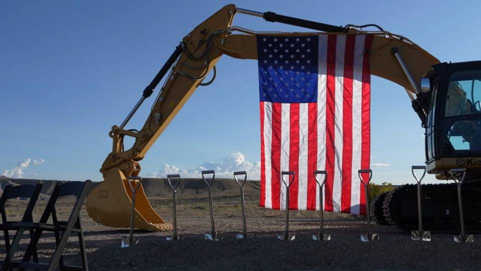 Valar公司USREL项目现场的金色破土动工铲摆放在Kiewit挖掘机上,与悬挂的美国国旗形成鲜明对比。(来源:Valar Atomics)