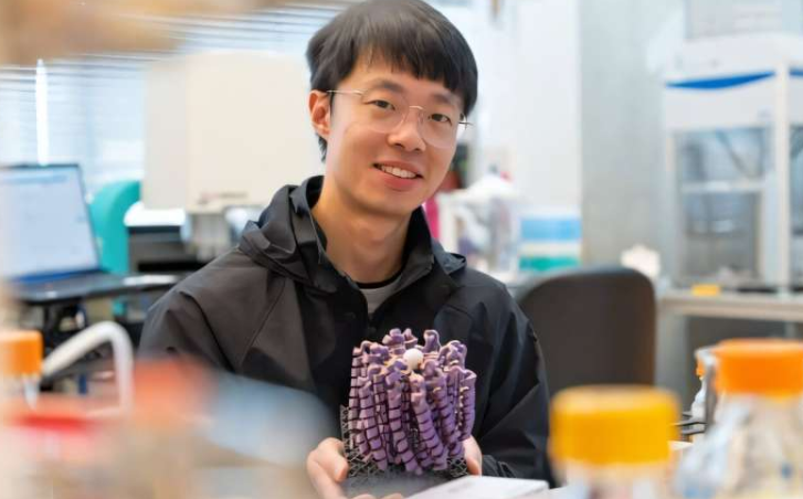 蛋白质设计研究员刘玉来(音译)手持一个放大的3D打印模型,该模型是其团队从零开始设计功能性钙通道的成果。他站在华盛顿大学医学院蛋白质设计研究所大卫·贝克(David Baker)的实验室里。